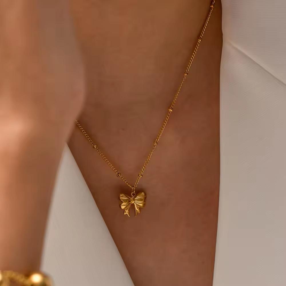 A close-up image of a gold bow-shaped necklace on a person's skin, highlighting the design and shine of the jewelry.